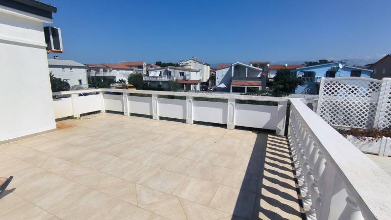The terrace of a family house in Vrsi with a view of the surrounding buildings and the blue sky.