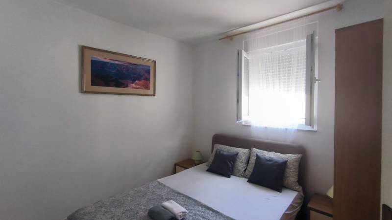 A bedroom in a family house with a bed, a painting, and an open window.