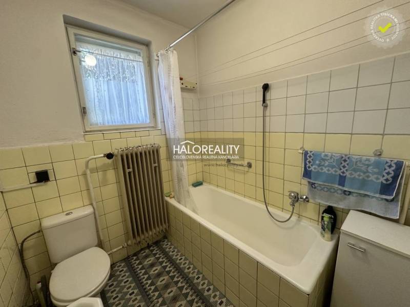 Bathroom in a family house with a bathtub, radiator, and window, decorated with tiles.