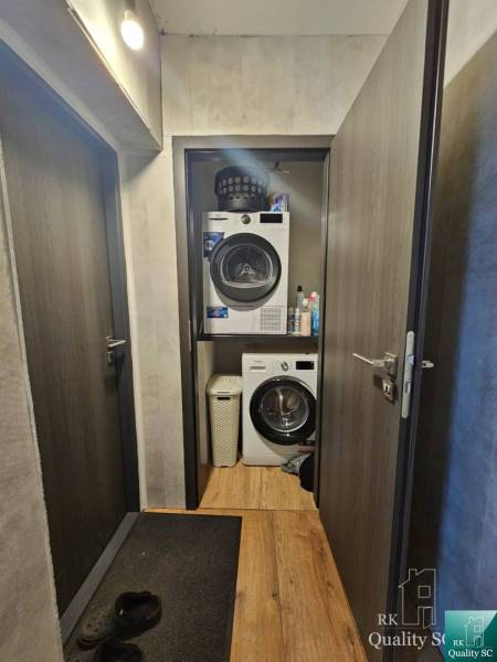 A narrow hallway in a family house with a washing machine and dryer, wooden floor, and dark doors.