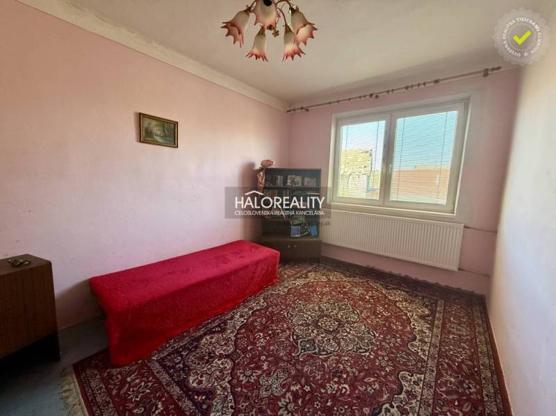 A room in a family house with a carpet, a sofa, a window, and a painting on the wall.
