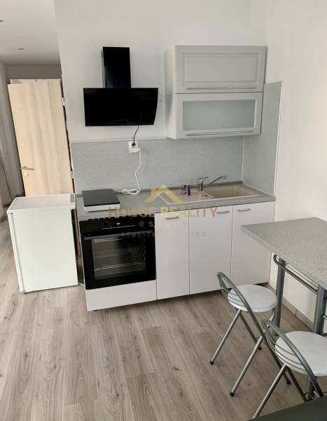 A kitchenette with a sink, stove, and a small dining table in a 2-room apartment.