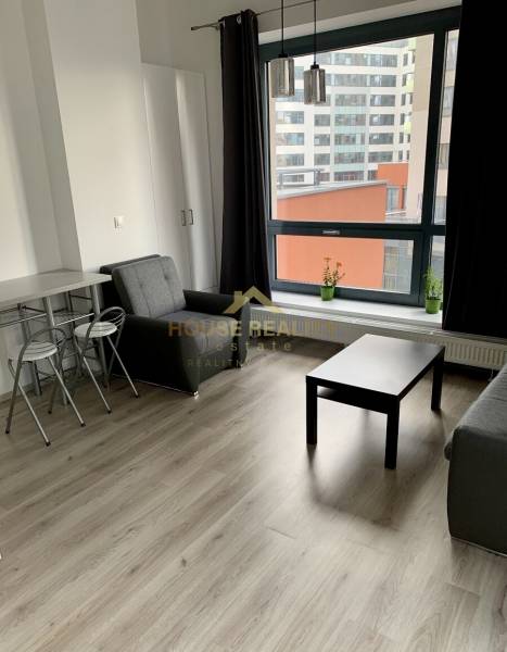 Living room of a two-room apartment with a seating area, table, and view of city buildings.