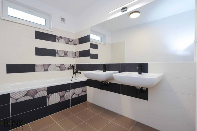 A bathroom in a 3-room apartment with a bathtub, two sinks, and black-and-white tiles.