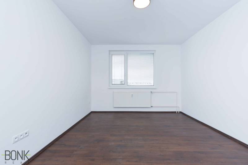 A room with white walls, a dark floor, and a window in a 3-room apartment.