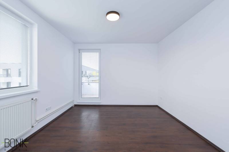 An empty room with a dark floor and a window in a 3-room apartment.