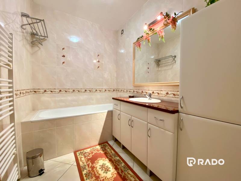 A bathroom in a 3-room apartment with a bathtub, cabinets, and a mirror with flowers.