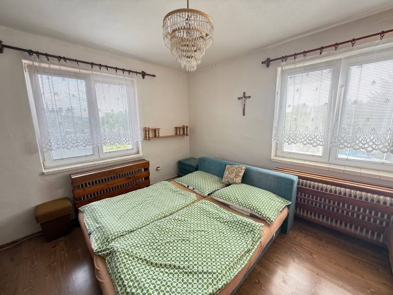 Spálňa v rodinnom dome s dvojitými oknami, posteľou a lusterom.