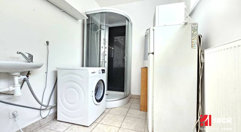 A bathroom in a studio apartment with a shower, washing machine, and refrigerator.
