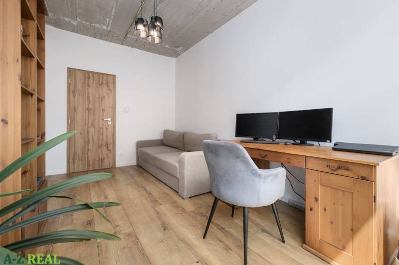 A study in a 4-room apartment with a desk, computers, and a gray chair, wooden floor.