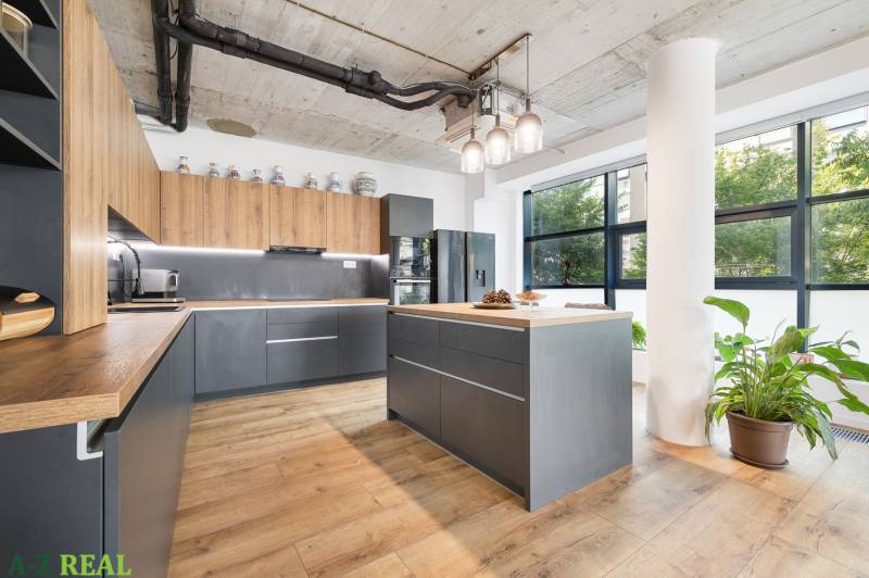 The kitchen of a 4-room apartment with gray and wooden cabinets, large windows, and a plant.