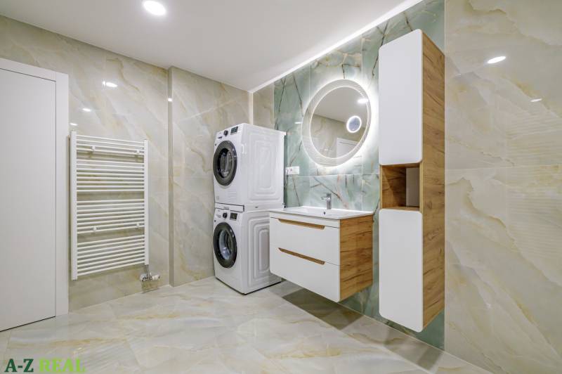 Spacious bathroom with a washing machine, dryer, round mirror, and built-in furniture in a 4-room apartment.