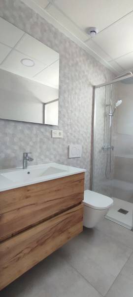 A bathroom in a 4-room apartment with a wooden cabinet, a shower corner, and a mirror.
