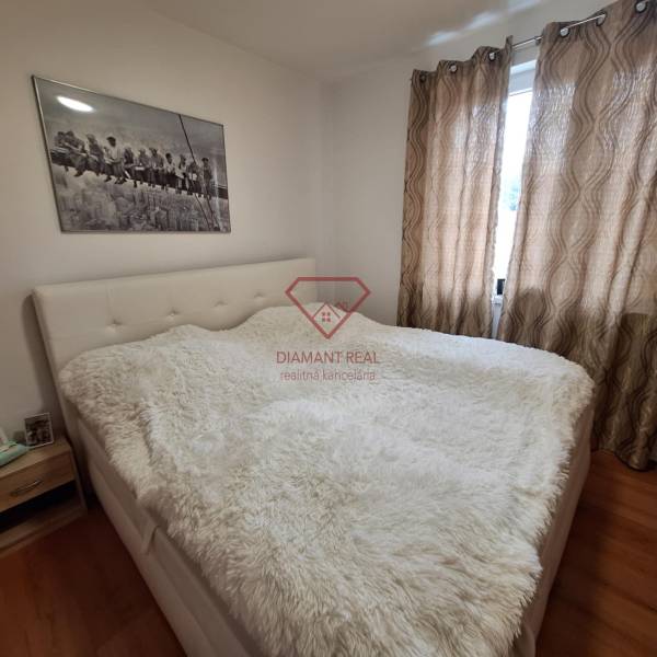 A bedroom in a 3-room apartment with a light bed, blackout curtains, and a painting on the wall.