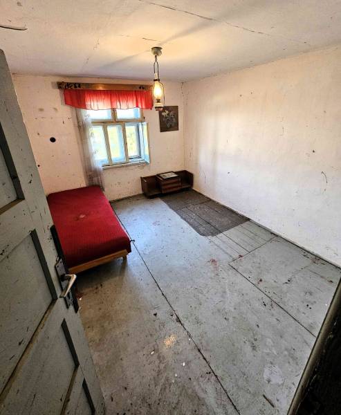 A simple room with a bed in a family house, wooden floors, curtains on the window.