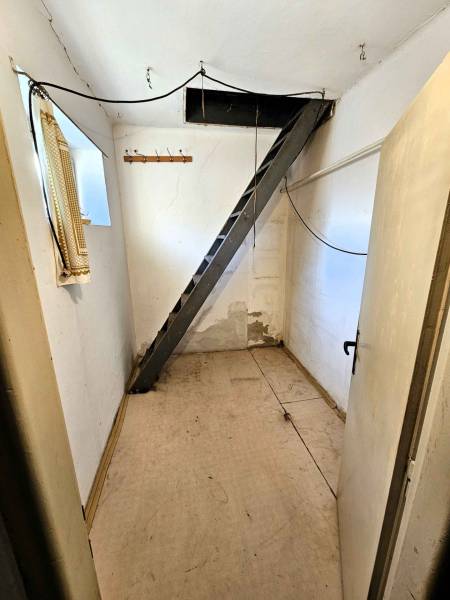A narrow hallway with a metal ladder, a coat rack, and white walls in a family house.