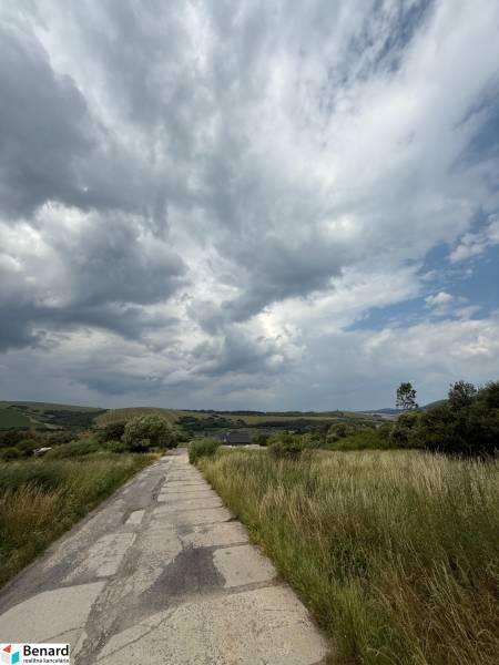 A country road leading through green fields in Ľubotín under a dramatic sky.