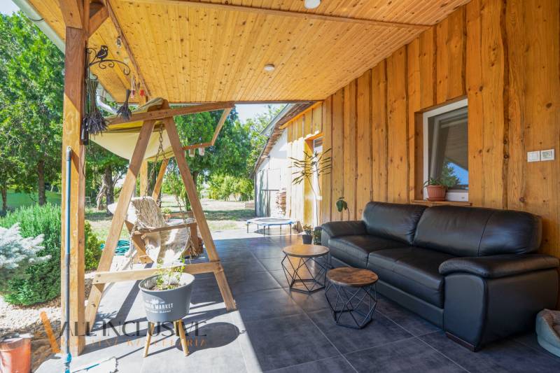 The terrace of a family house in Tvrdošovce with wooden paneling, a swinging bench, and a black sofa.