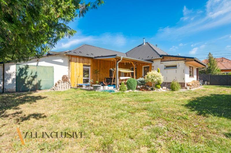 A family house in Tvrdošovce with wooden cladding, a garden, and a view of the blue sky.