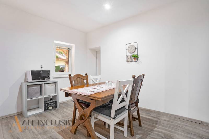 Dining room in a family house with a wooden table and chairs, white wall, and decoration.