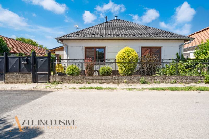 A family house in Tvrdošovce with a modern roof, landscaped garden, and wrought iron fence.