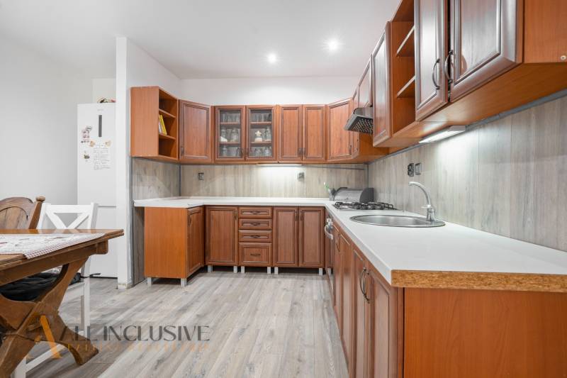 A kitchen in a family house with a light floor and wooden cabinets.