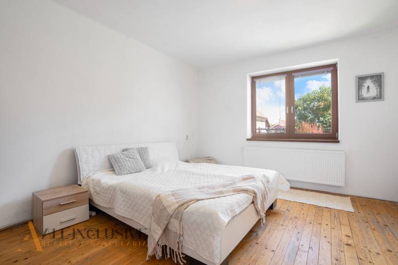 Bright bedroom in a family house with a white bed and wooden floor.
