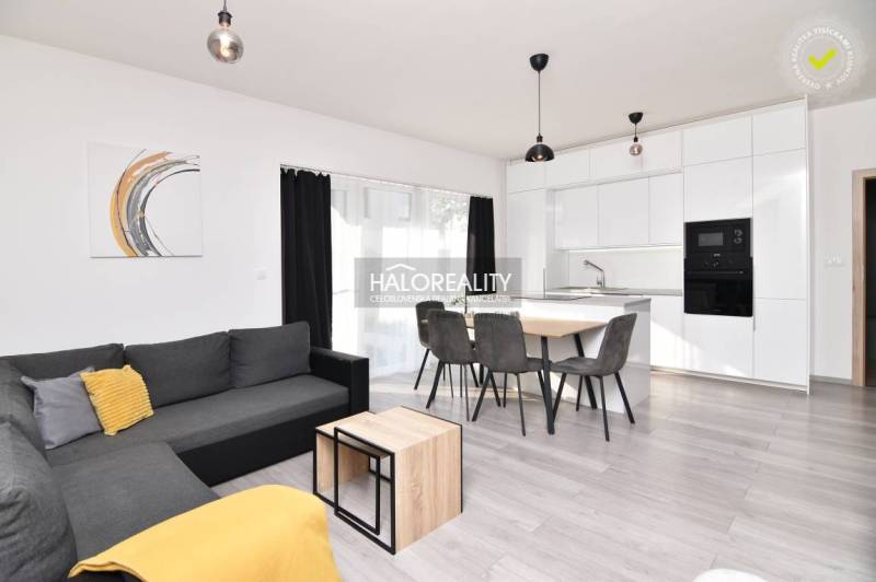 Living room in a family house with a gray sofa, dining table, and white kitchen.