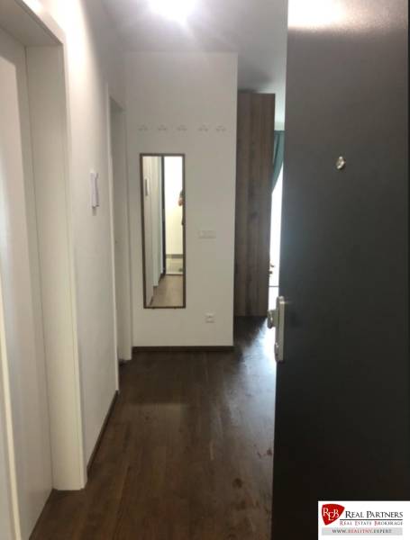 A hallway in a 2-room apartment with a wooden floor and a mirror on the wall.