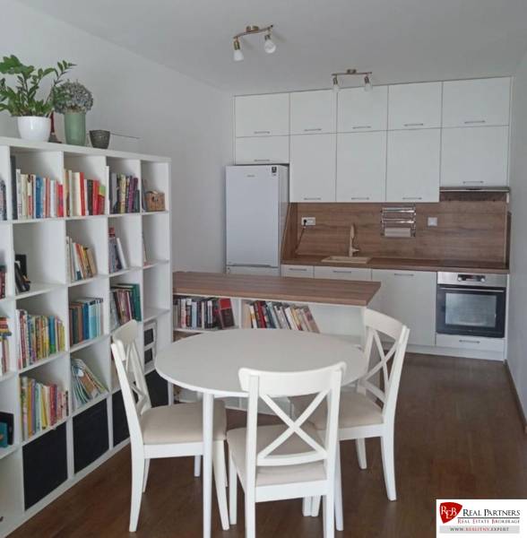 A kitchen in a 2-room apartment with a dining table, a bookshelf, and built-in appliances.