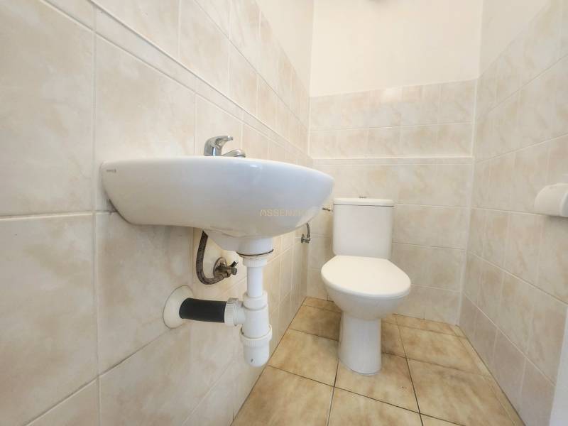 Bathroom with a toilet and sink, tiled with light tiles. Commercial premises.