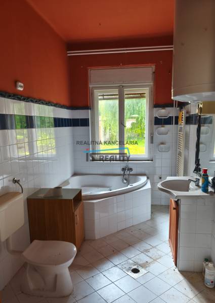 The bathroom with a bathtub and a sink in the family house has orange walls and white tiles.