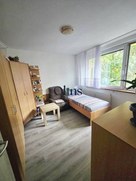 A room in a 2-room apartment with a bed, a cabinet, an armchair, and large windows.