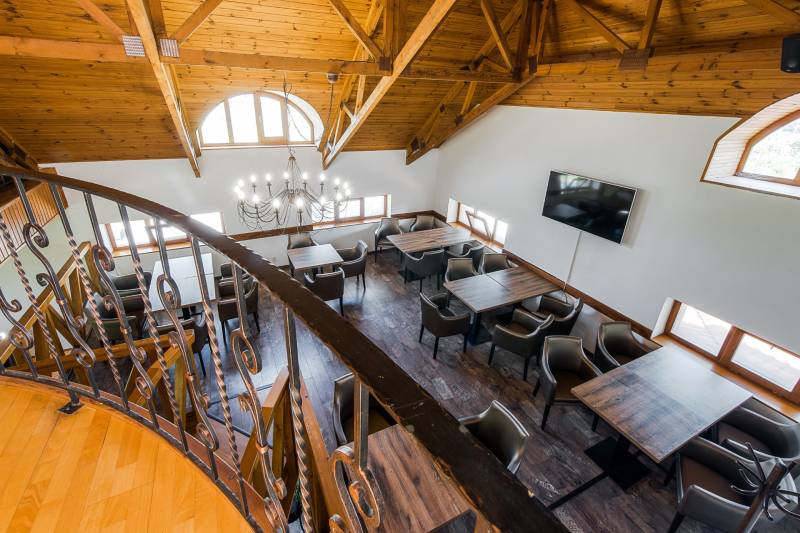 Gastro premises with a wooden ceiling, chandelier, and metal railing, comfortable seating at tables.