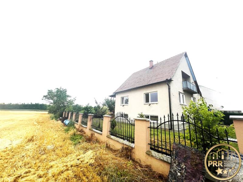 A family house in Veľké Chlievany near a field with a fence and a garden in the background.