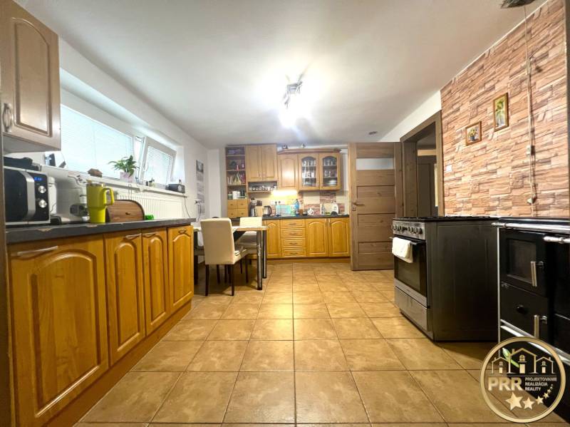 A kitchen in a family house with wooden cabinets, tiles, and a dining table.