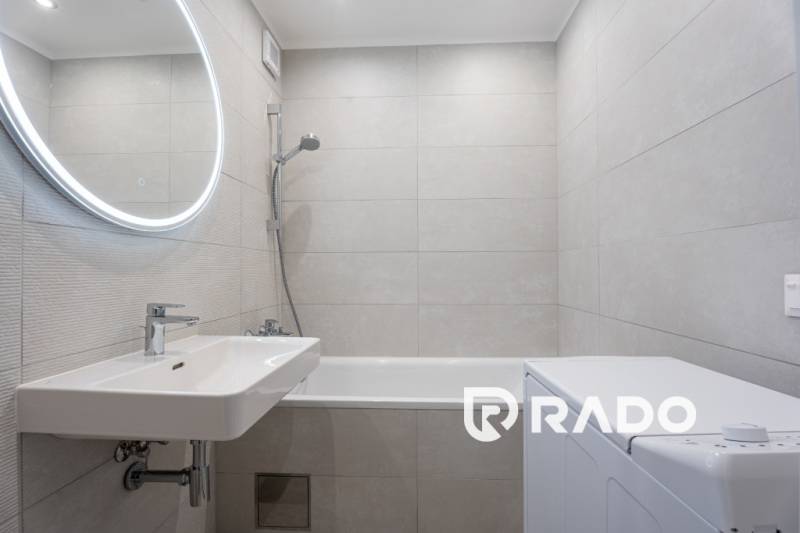 A bathroom in a 3-room apartment with a mirror, bathtub, and washing machine.