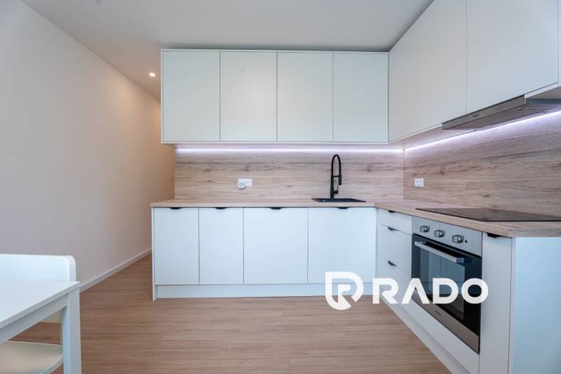 A modern kitchen in a 3-room apartment with white cabinets and a black faucet.