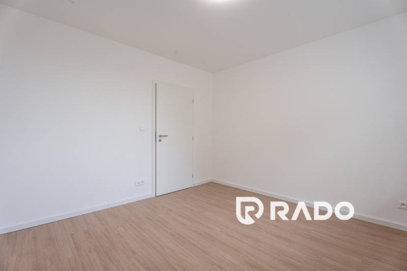 An empty room with wooden flooring and white walls in a 3-bedroom apartment.