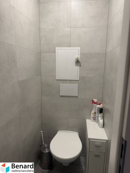 A toilet in the bathroom of a one-room apartment with ceramic tiles and storage furniture.
