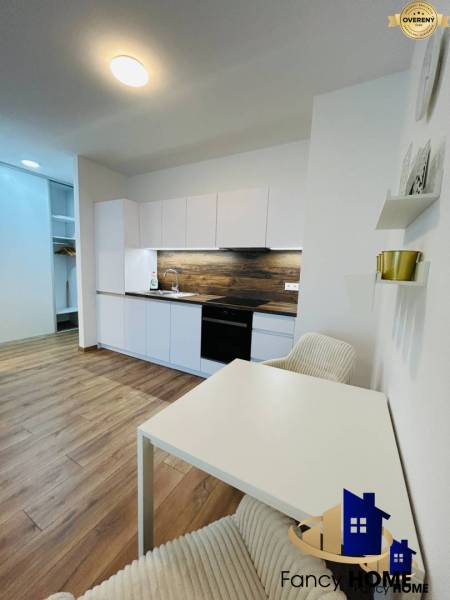 A kitchen corner with a wooden floor and white furniture in a studio apartment.