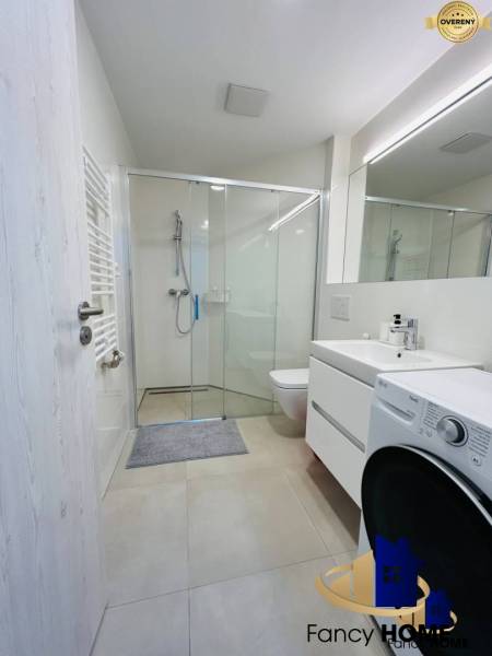 A bathroom in a studio apartment with a modern shower and a washing machine.