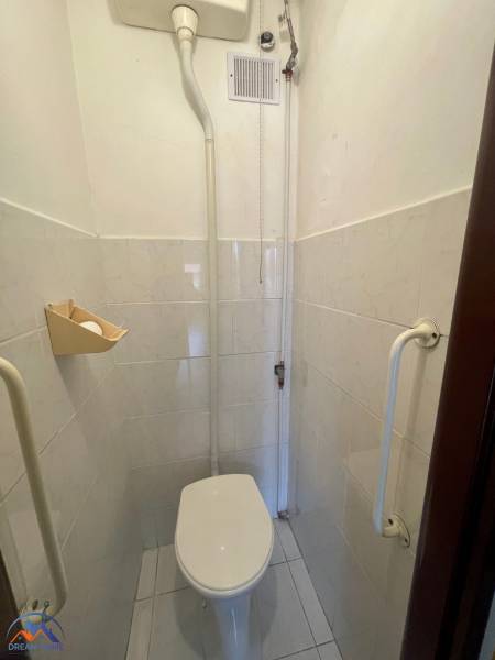 Small toilet in a 3-room apartment with tiled walls and a handle.
