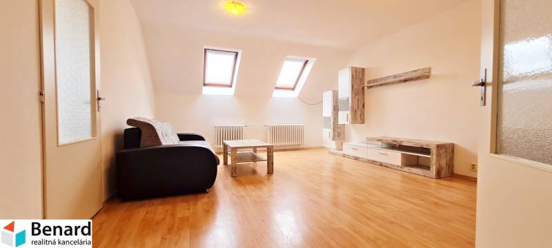 A bright room with a wooden floor, a sofa, and furniture under skylights in the building.