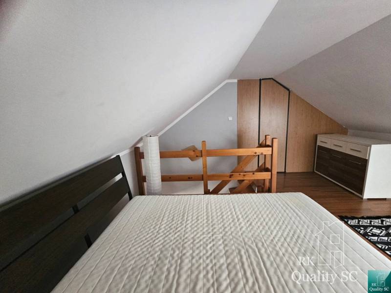 Attic bedroom with a sloped ceiling in a 3-room apartment, with a wooden railing and a dresser.