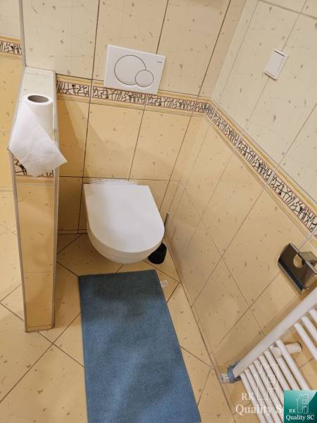A toilet with tiled walls, a blue mat, and a radiator in a 3-room apartment.