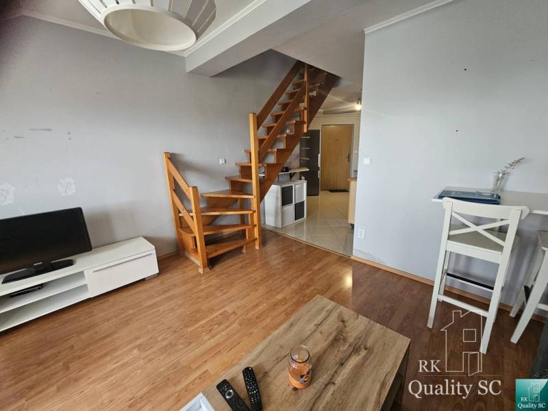 Interior of a 3-room apartment with a staircase and wooden floors, TV stand and table.