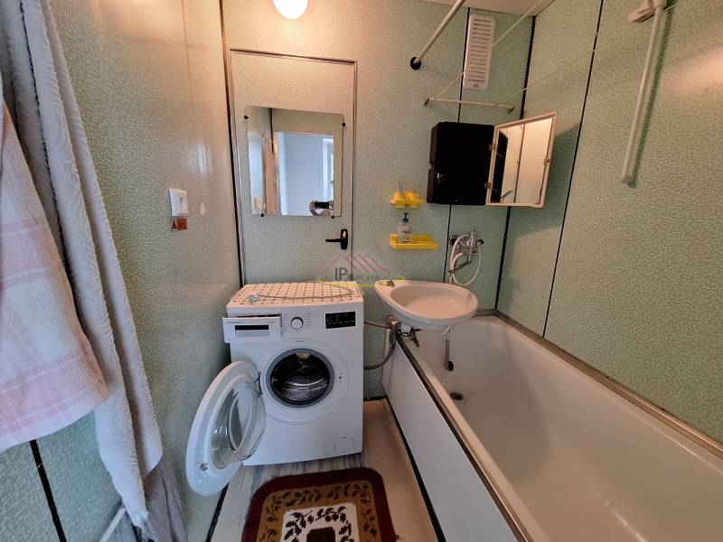 Bathroom in a 3-room apartment with a washing machine, bathtub, and mirror on the wall.