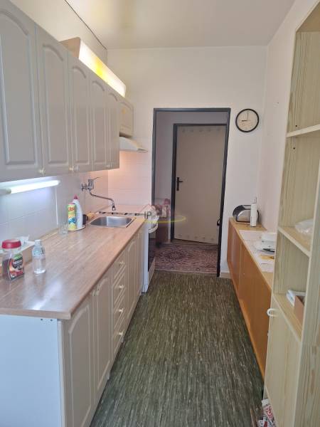 A kitchen in a 3-room apartment, with a wooden cabinet, a sink, and a clock on the wall.