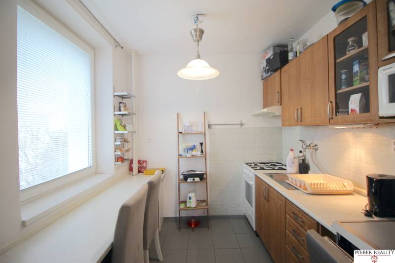 A kitchen with wooden cabinets, a gas stove, and white seating in a 3-room apartment.